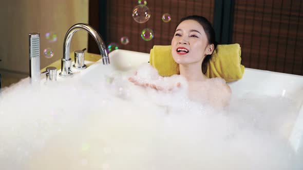 woman takes a bath and blowing soap bubbles in bathtub