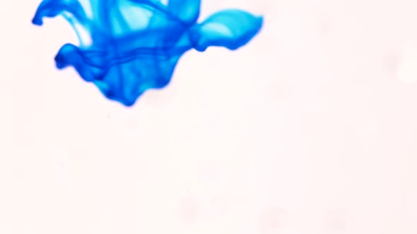 Slow motion footage of drops of blue coloring oozing and flowing into clear liquid