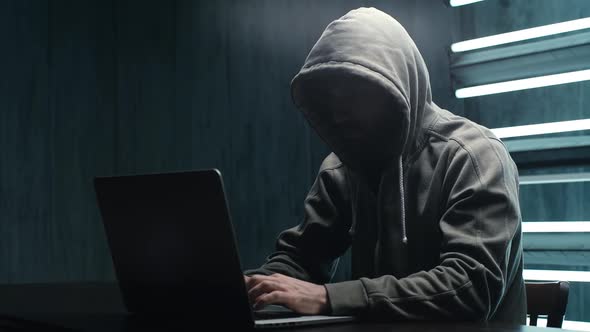 Unrecognizable Man Hacker Wearing Sweatshirt with Hood Typing on Laptop and Breaking Password