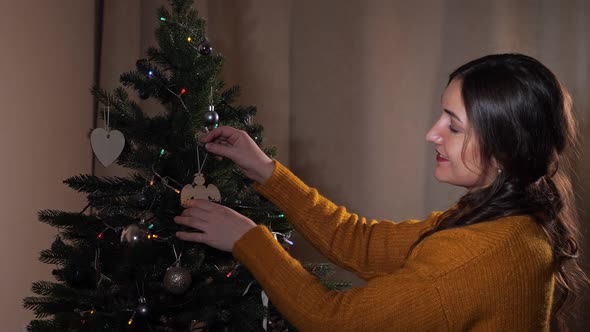 Beautiful Young Woman Decorates an Artificial Fir Tree with Toys