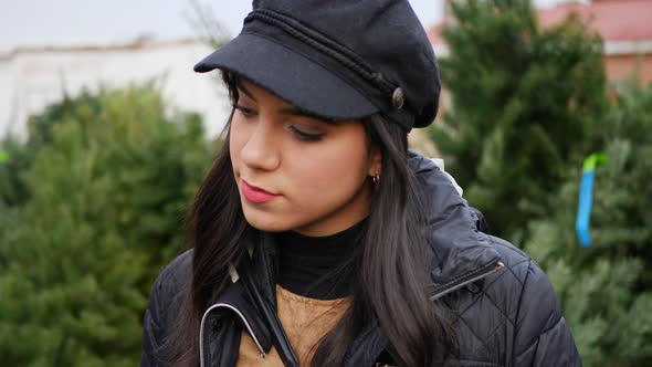 A beautiful hispanic woman shopping on a Christmas tree lot with green douglas fir conifers in a hol