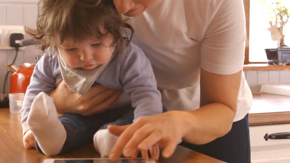 Mother using digital tablet while varrying her baby