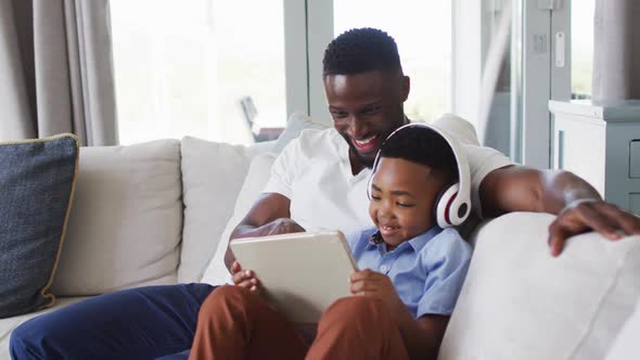 African american father and son using a digital tablet together with boy wearing headphones