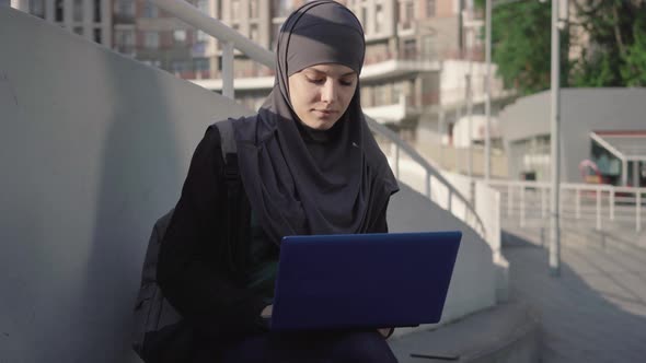 Portrait of Concentrated Young Woman in Hijab Opening Laptop and Typing on Keyboard. Focused Middle