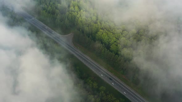 Aerial View of Driving Cars on the Road in the Forest Through the Clouds