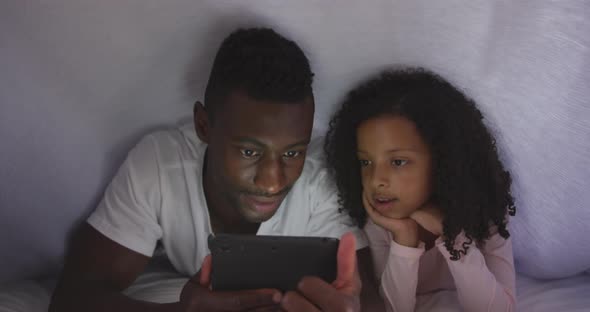 African american father and daughter looking at phone in bed