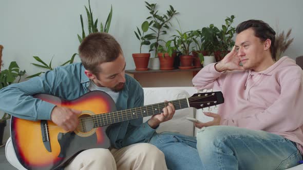 A Lgbt Man is Playing Guitar for His Boyfriend While Another One is Nodding Head for Music and