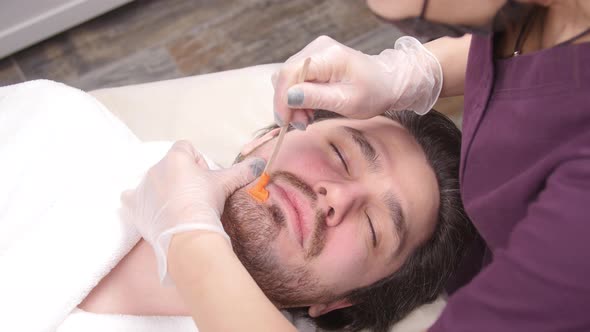 Concept of Cosmetology and Facial. A Woman Beautician Makes Face and Beard Modeling for a Man Waxing