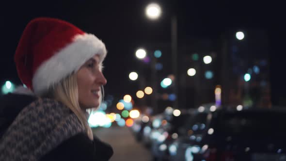 A beautiful woman in a Santa Claus hat walks at night on Christmas