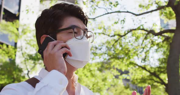 Asian man wearing face mask talking on smartphone on the street