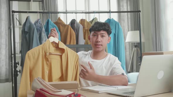Asian Man Online Seller Recommending A Shirt While Using Computer For Selling Clothes At Home