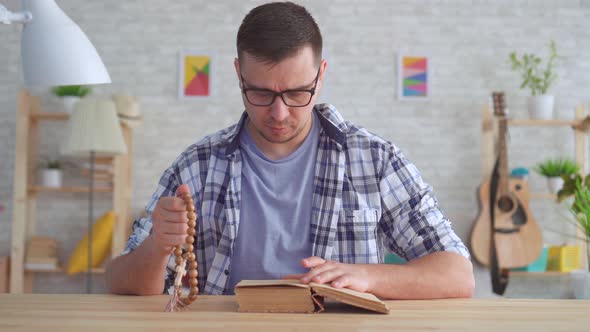 Portrait Young Man with Glasses with a Rosary in His Hands and Reading the Bible