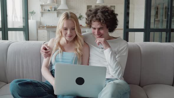 Happy Millennial Caucasian Couple Looking at Computer Screen Discussing Purchases in Online Store