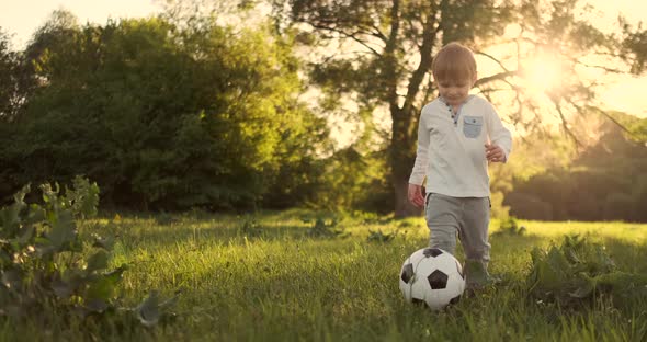 Happy Boy Running with Soccer Ball Running at Sunset in Summer Field