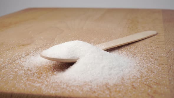 Heap of white granulated sugar on a wooden spoon on a cutting board.