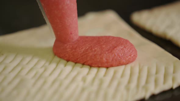 Squeezing pink strawberry cream from frosting piping bag on pastry, pastry dough filled with pink cr