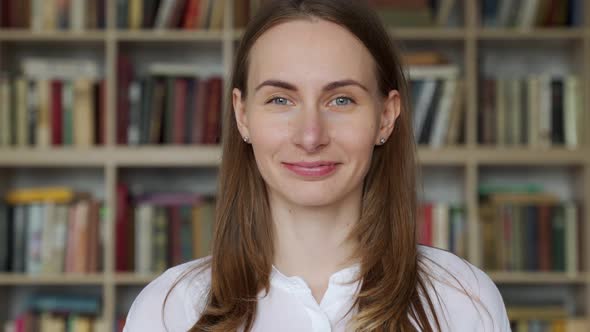 Portrait of Young Librarian Woman Smiling Looking at Camera in Library Bookshelf Background