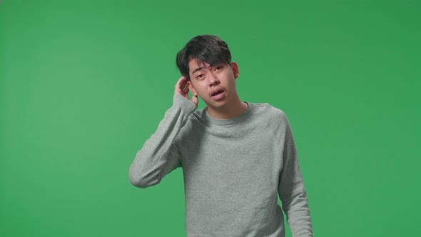 A Puzzled Asian Man Is Standing In Front Of Green Screen Background