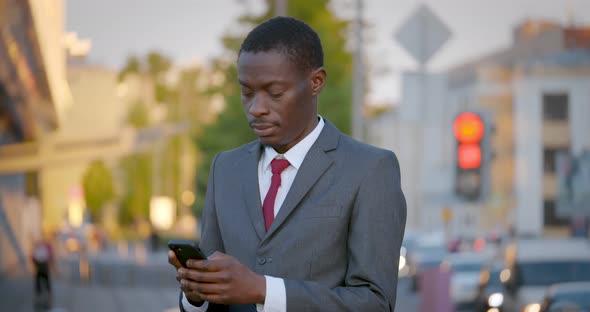 Bokeh Shot of Young Afro Businessman Using Mobile Phone Outdoors at Street