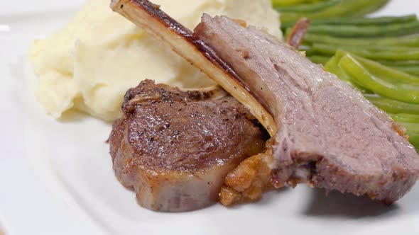 Slider Shot of Lamb Cutlets on a White Plate with Mashed Potato and Green Beans