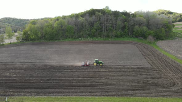 Farmer planting and fertilizing field at end of day. Mountain and small forest separate fields.