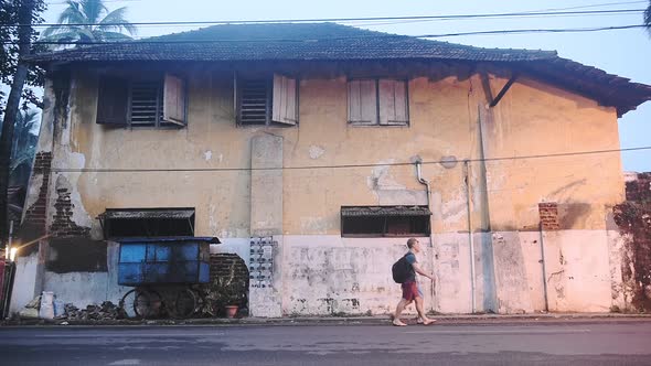 Two Caucasian Guys Passing By A Big Old House With Cracked Painted Walls In Kochi, India - Medium Sh