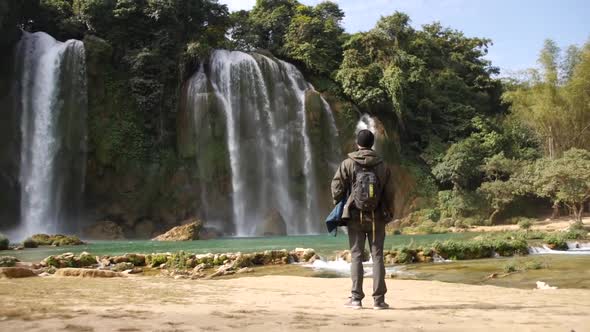 Traveller With Backpack Standing And Admiring The Water Flowing At Ban Gioc-Detian Falls (Cao Bang W