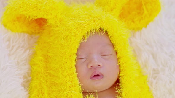 happy newborn baby weaing cute yellow egg costume lying sleep on grey carpet