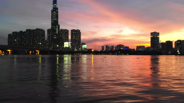 Vibrant twilight glow and city lights reflected in Saigon river surface; aerial