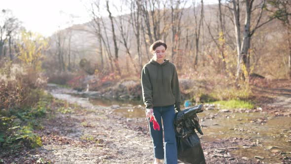 Portrait of a Beautiful Volunteer Girl in the Sun with a Plastic Bag in the Autumn Landscape