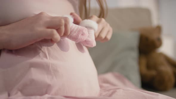 Pregnant Woman Playing With Tiny Pink Booties