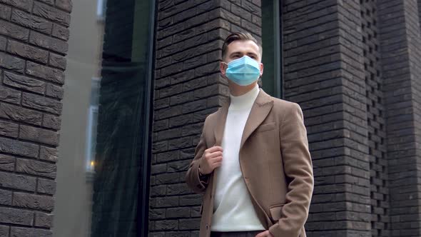 Elegant Businessman in Protective Medical Mask on the Street Near a Modern Office