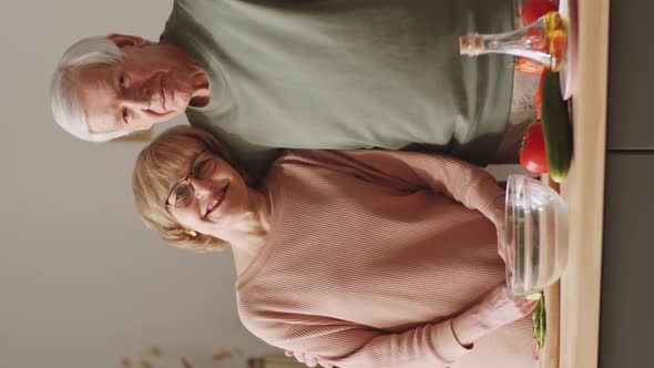 Romantic Senior Couple Cooking in Kitchen and Smiling at Camera