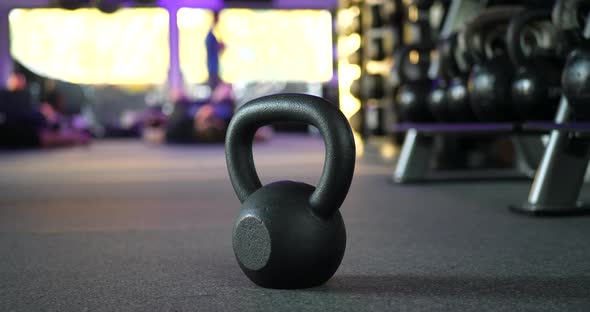 A kettlebell weight in a gym with people working out in a physical fitness training class in the bac