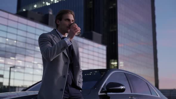 Handheld Portrait of a Elegant Businessman Standing Near a Business Car and Drinking Coffee Top