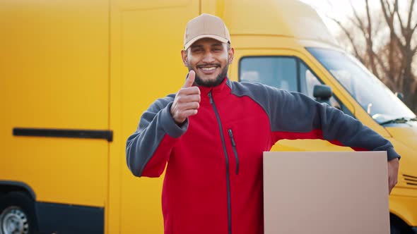 Delivery Boy Carrying A Cardboard Box  Making Thumbs Up Sign At The Camera