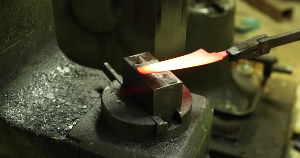 Bladesmith working with hot blade at hydraulic forge hammer