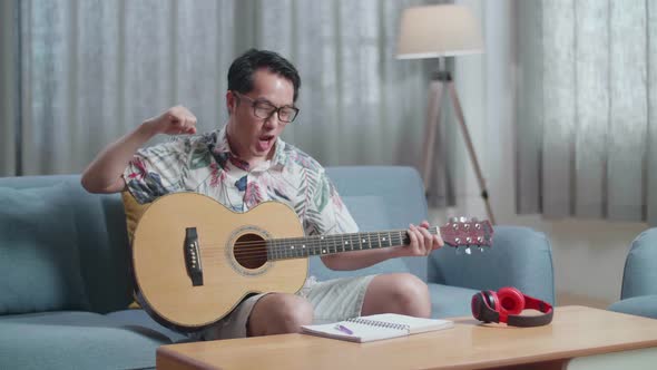 Asian Man Composer With A Guitar Celebrating For Finishing Composing Music On Paper At Home