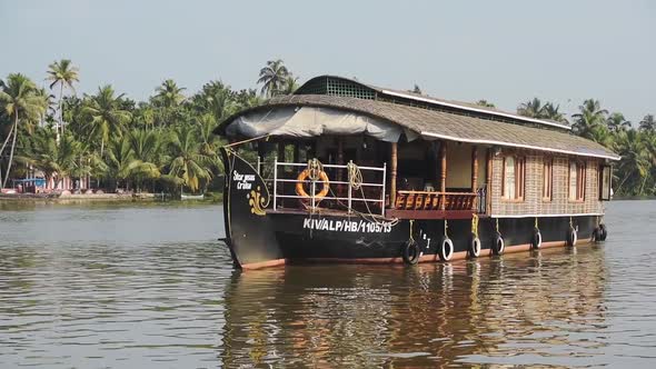 River side view of a houseboat passing by, with palm trees in the background, Kerala Backwaters, Ind