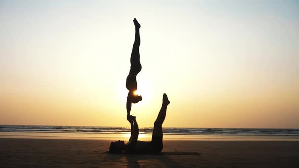 Fit Sporty Couple Practicing Acro Yoga with Partner Together on the Sandy Beach