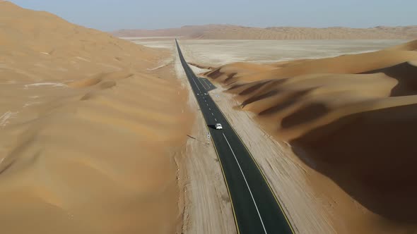 Aerial view of white car driving on road between dunes in the desert, Abu Dhabi.