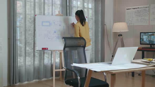 Asian Woman Engineer With A Laptop Drawing Blueprint On The Whiteboard At The Office alt