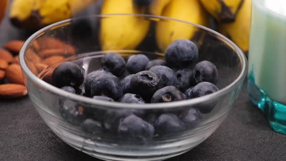 Drops Fresh Blue Berry in Bowl with Banana Milk and Almond on Table
