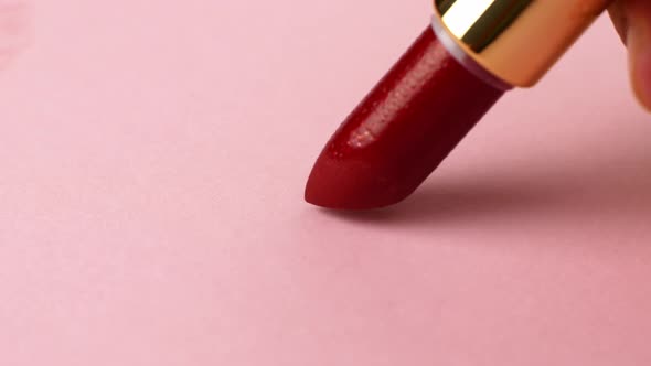 Woman paints with red lipstick on pink paper. Drawing hearts on paper.