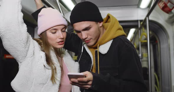 Millennial Couple Talking and Looking at Mobilephone Screen. Pretty Girl and Her Boyfriend Sharing