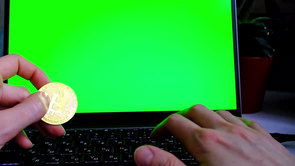 A bitcoin gold coin in hand on a laptop on the background of a laptop monitor with a green chromakey