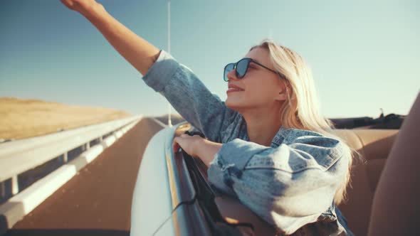 Happy Woman in Sunglasses Enjoys Life Ride in Cabriolet Raising Her Hands to Sky