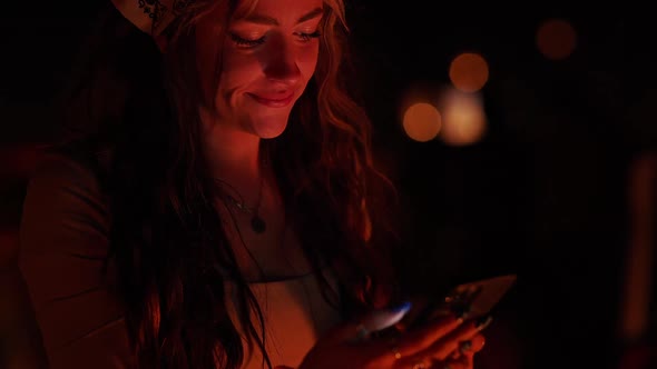 Young woman flipping through her phone while she is near a fire