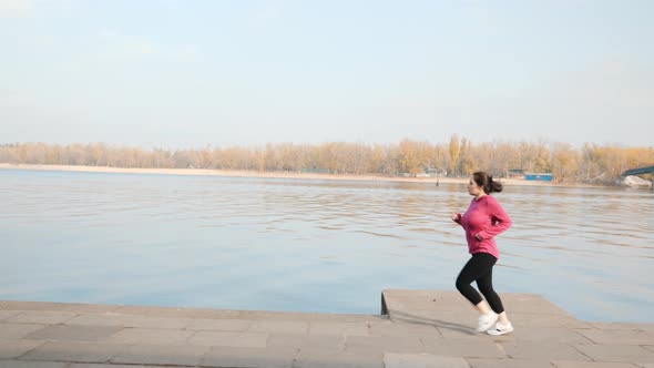 Chubby young woman running in city promenade as a part of weight loss program. Running concept