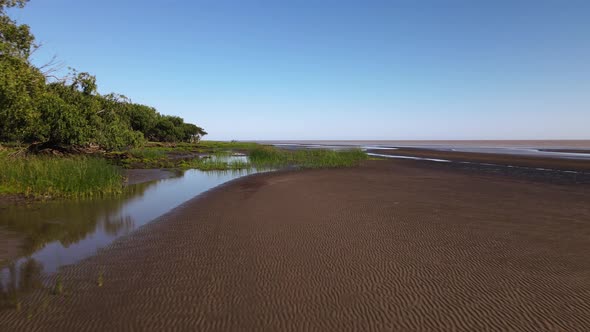 Low forward aerial of sand banks and reeds by bank of Rio de la Plata